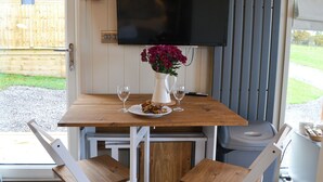Een gezellig eetgedeelte met een houten tafel, twee stoelen, een witte vaas met bloemen en een aan de muur bevestigde televisie.