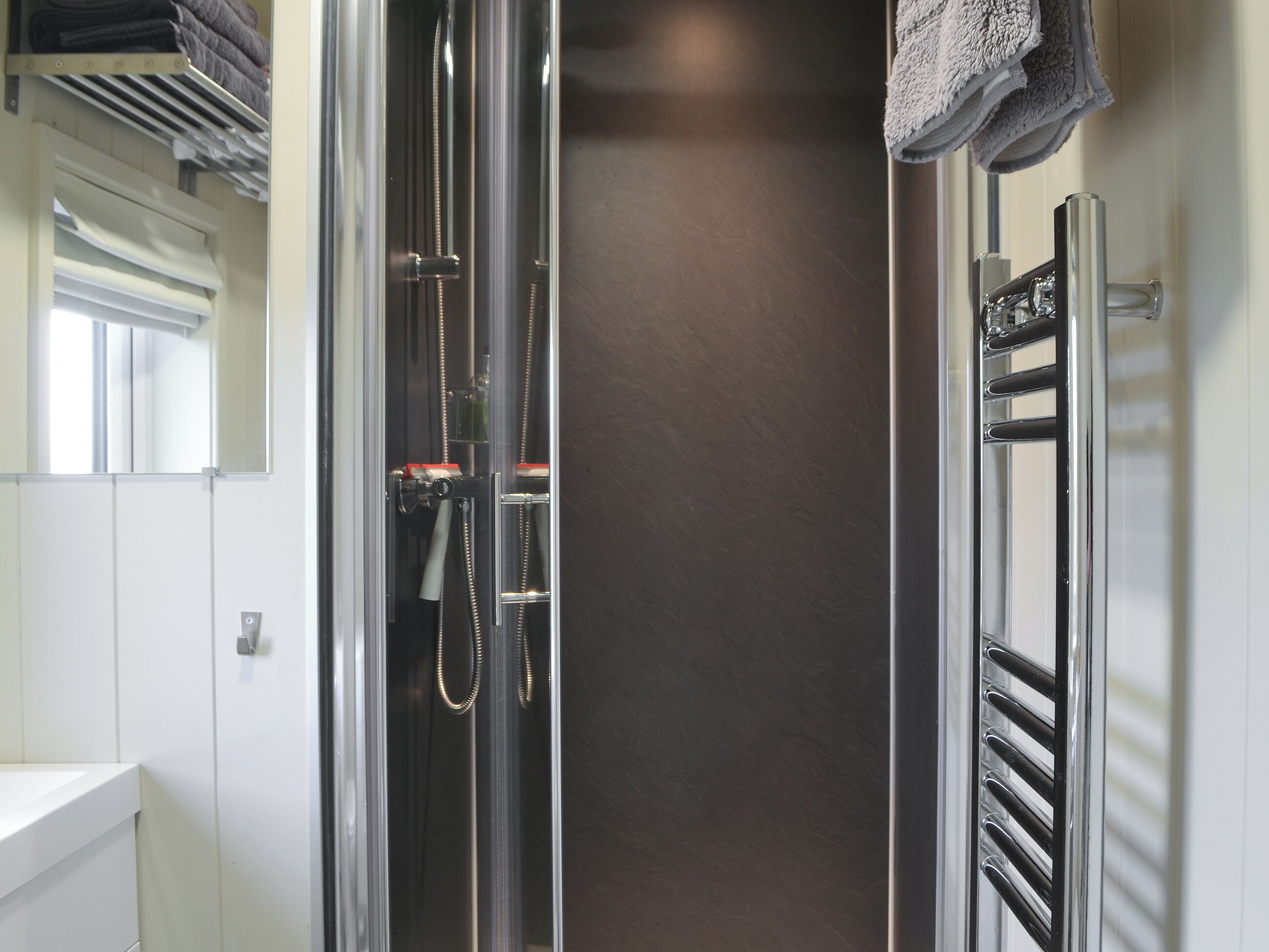 A modern bathroom with a glass-enclosed shower, a white sink, and a towel rack.