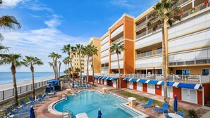 Zona de piscina de hotel con varias sillas de descanso y sombrillas, una piscina grande y vistas a la playa.