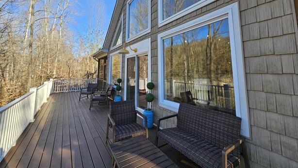 A wooden deck with outdoor furniture and large windows overlooking a forested area. - Welcome to Hidden Haven – A Spacious Lakeside Retreat (Burnside)