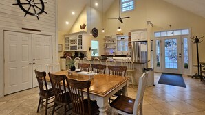 A spacious kitchen with a dining area, featuring a large wooden table, multiple chairs, a ship's wheel decoration, and a modern refrigerator. - Welcome to Hidden Haven – A Spacious Lakeside Retreat (Burnside)