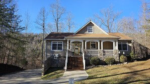 A two-story house with a stone foundation, a front porch, and a driveway leading to the entrance. - Welcome to Hidden Haven – A Spacious Lakeside Retreat (Burnside)