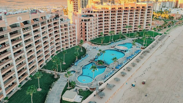 Hotel alt, amb múltiples balcons, una piscina central i una zona de platja.