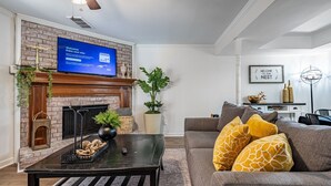 Una sala de estar con chimenea, un televisor montado encima, un sofá con cojines estampados y una mesa de centro con adornos.