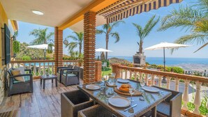 A terrace with wicker furniture, a table set for dining, and a view of the sea.