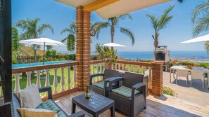 A covered outdoor patio with wicker furniture, a pool, and a view of the ocean.