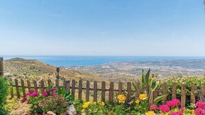 A wooden fence with flowering plants in the foreground and a coastal landscape in the background.