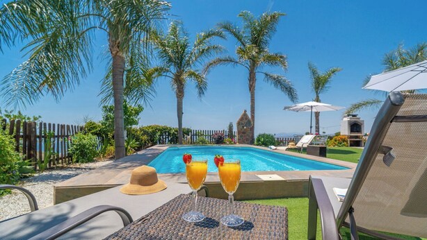 A poolside area with a table, two glasses of orange juice, a straw hat, and a lounge chair.