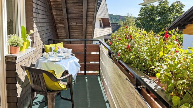 Ein Balkon mit Tisch für Zwei, Blumentöpfen und Geländer aus Holz.