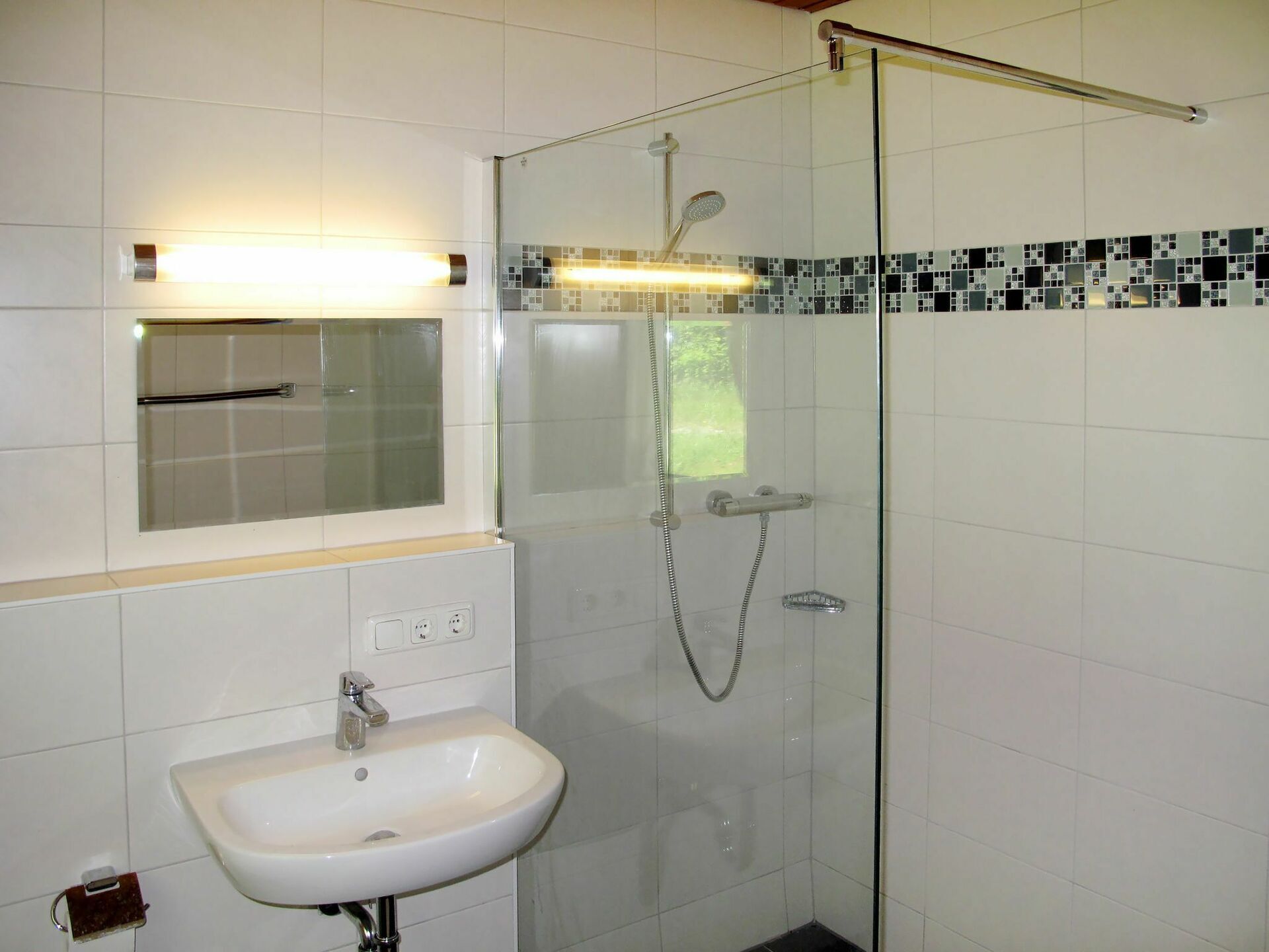 Une salle de bain avec une douche à parois de verre, un lavabo blanc et un miroir au-dessus.