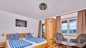 A room with a wooden bed, a small round table, a grey armchair, and a window with a view of the countryside. - Stunning private villa for 17 guests with pool, WIFI, TV, terrace and pets allowed (Baierweg)