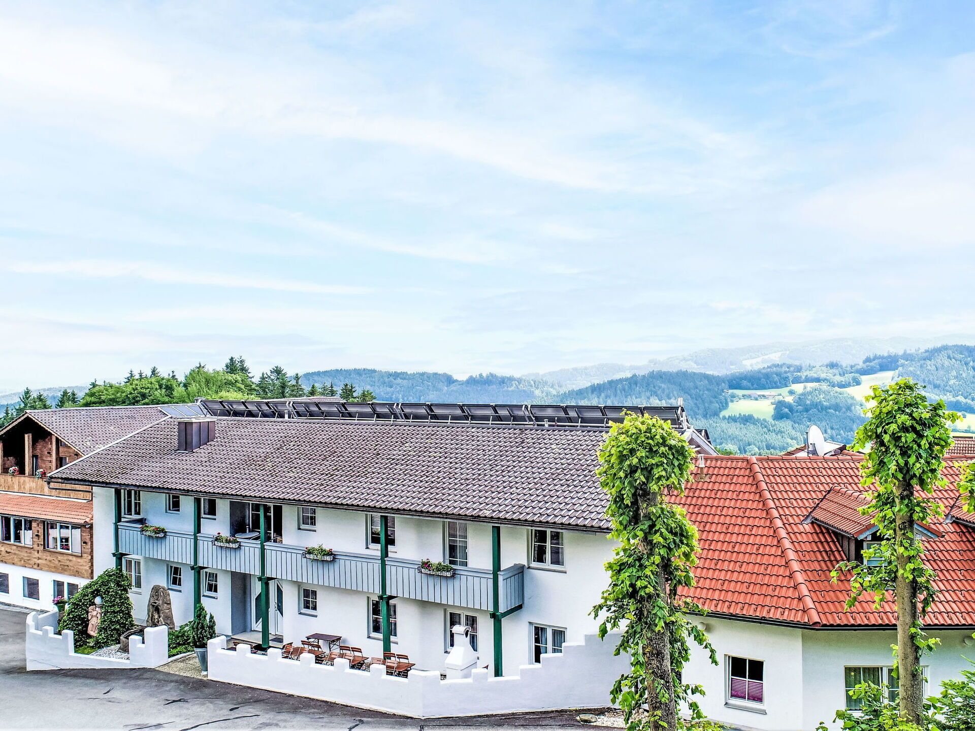Un immeuble à plusieurs étages, doté d’un toit recouvert de tuiles, de balcons ornés de plantes et offrant une vue sur un paysage montagneux.