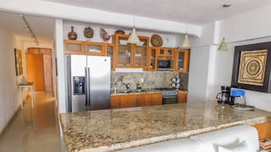 A modern kitchen with granite countertops, stainless steel appliances, wooden cabinets, and pendant lighting.