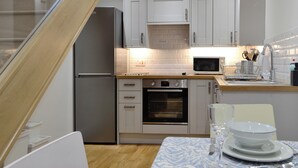 A modern kitchen with white cabinets, a stainless steel refrigerator, a microwave, and a built-in oven. - Cornel Clyd (Cosy Corner) (Felinfach, near Lampeter)