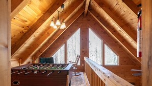 Una habitación acogedora en el ático con una mesa de fútbol, ventanas amplias y techo de madera.