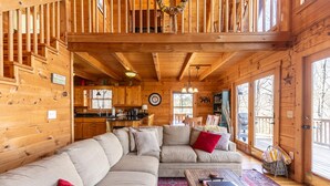 Interior de una cabaña de madera con un sofá grande en forma de L, un comedor y una cocina.
