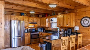 Interior de una cabaña de madera con cocina que cuenta con electrodomésticos de acero inoxidable, armarios de madera y una isla central con taburetes de bar.