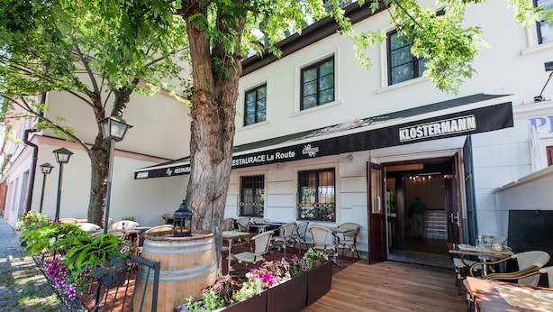 A restaurant with outdoor seating, wooden tables, and planters with flowers. - Penzion La Route (Prague)