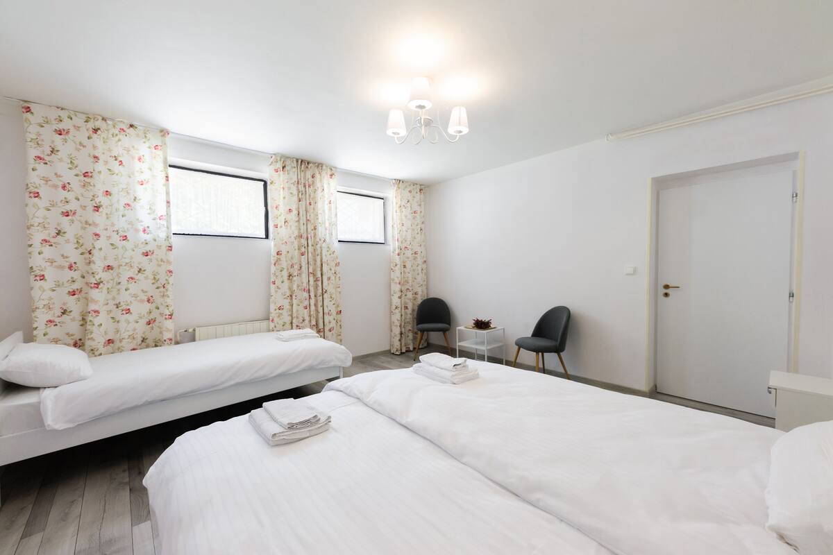 A hotel room with two single beds, a small table with chairs, and a door.