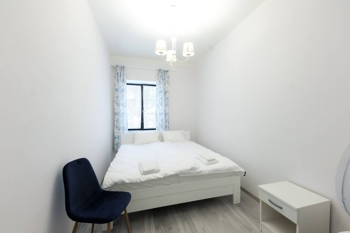 A bedroom with a bed, a chair, a bedside table, and a window with curtains.