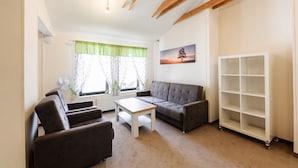 A living room with a sofa, two armchairs, a coffee table, a white shelving unit, and a window with curtains. - Penzion La Route (Prague)