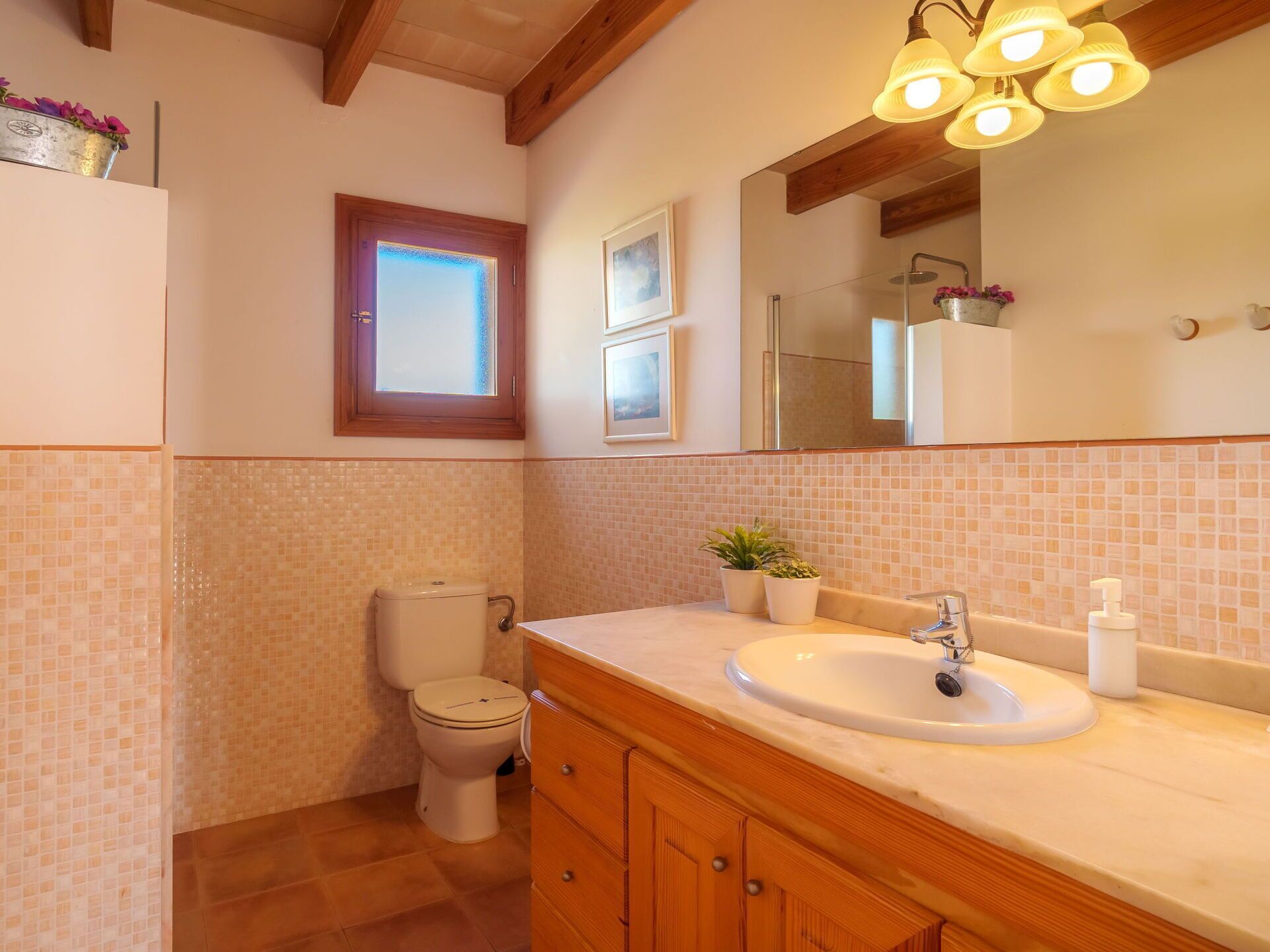 A bathroom with a toilet, sink, wooden cabinets, a mirror, and a window with a view.