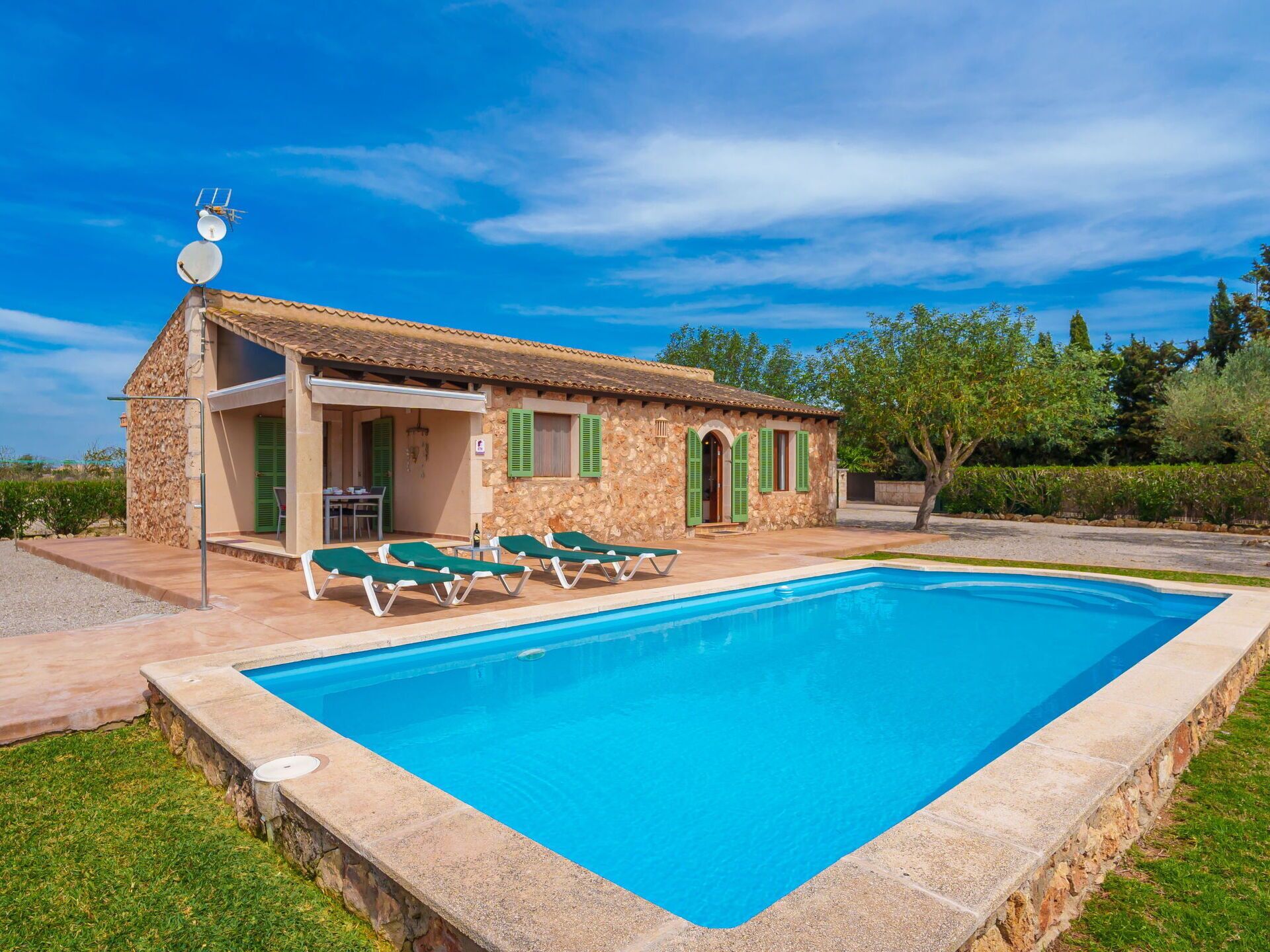 A stone building with a swimming pool, green shutters, and lounge chairs.