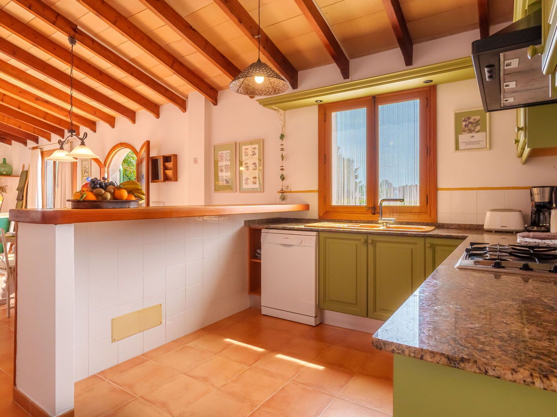 Une cuisine avec un plafond en bois, un îlot central doté d’un évier et une fenêtre avec des stores.