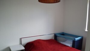 Quarto pequeno com uma cama de casal, uma mesa de cabeceira branca e um móvel de armazenamento azul.