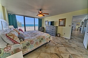 A bedroom with a large bed, a ceiling fan, a dresser, a TV, and a view of the ocean. - Seachase W 101 2 Bedroom 2 Bath unit. Beach Chair Service for 4 Included (Panama City Beach)