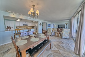 A spacious living area with a dining table, comfortable seating, a chandelier, and a view through large windows. - Seachase W 101 2 Bedroom 2 Bath unit. Beach Chair Service for 4 Included (Panama City Beach)