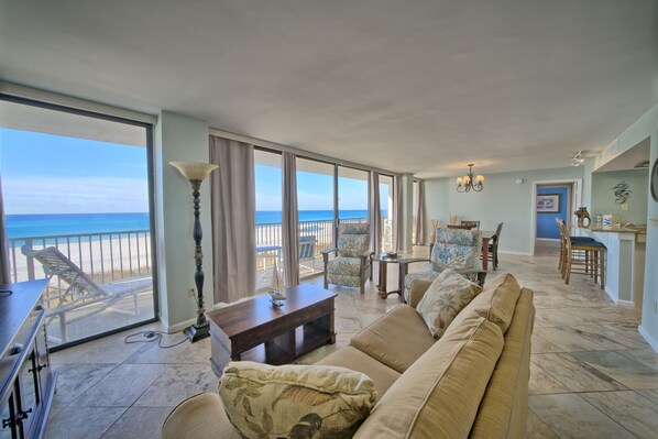 A spacious living area with a large window overlooking the beach, a sofa, a coffee table, and a dining area. - Seachase W 101 2 Bedroom 2 Bath unit. Beach Chair Service for 4 Included (Panama City Beach)