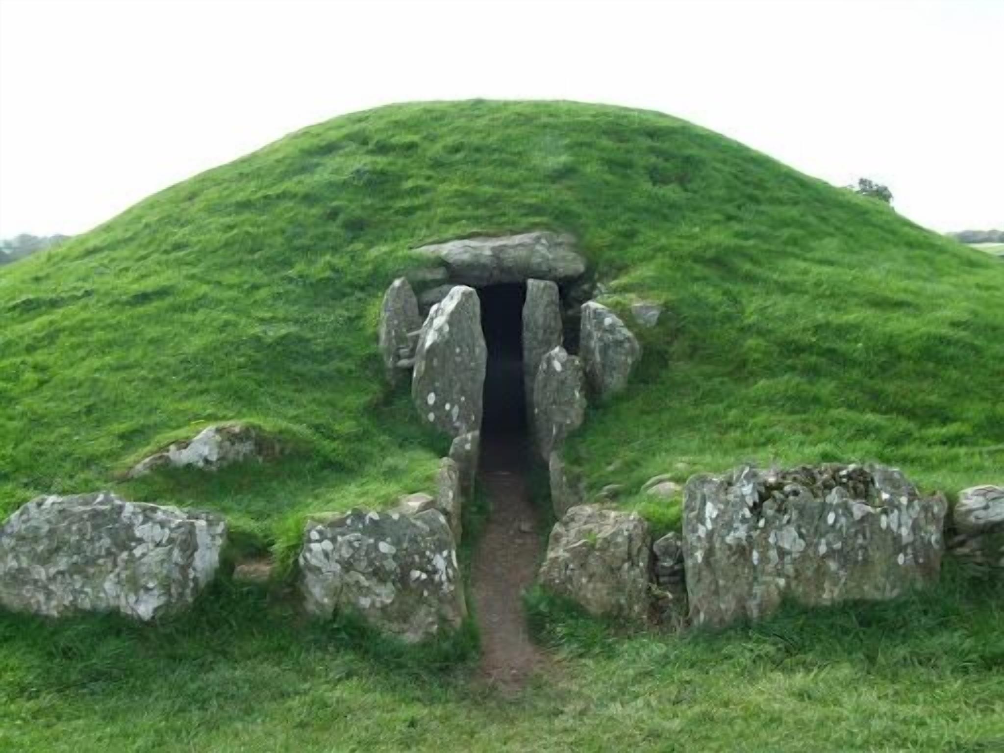 A mound with a stone entrance, surrounded by grass and rocks.