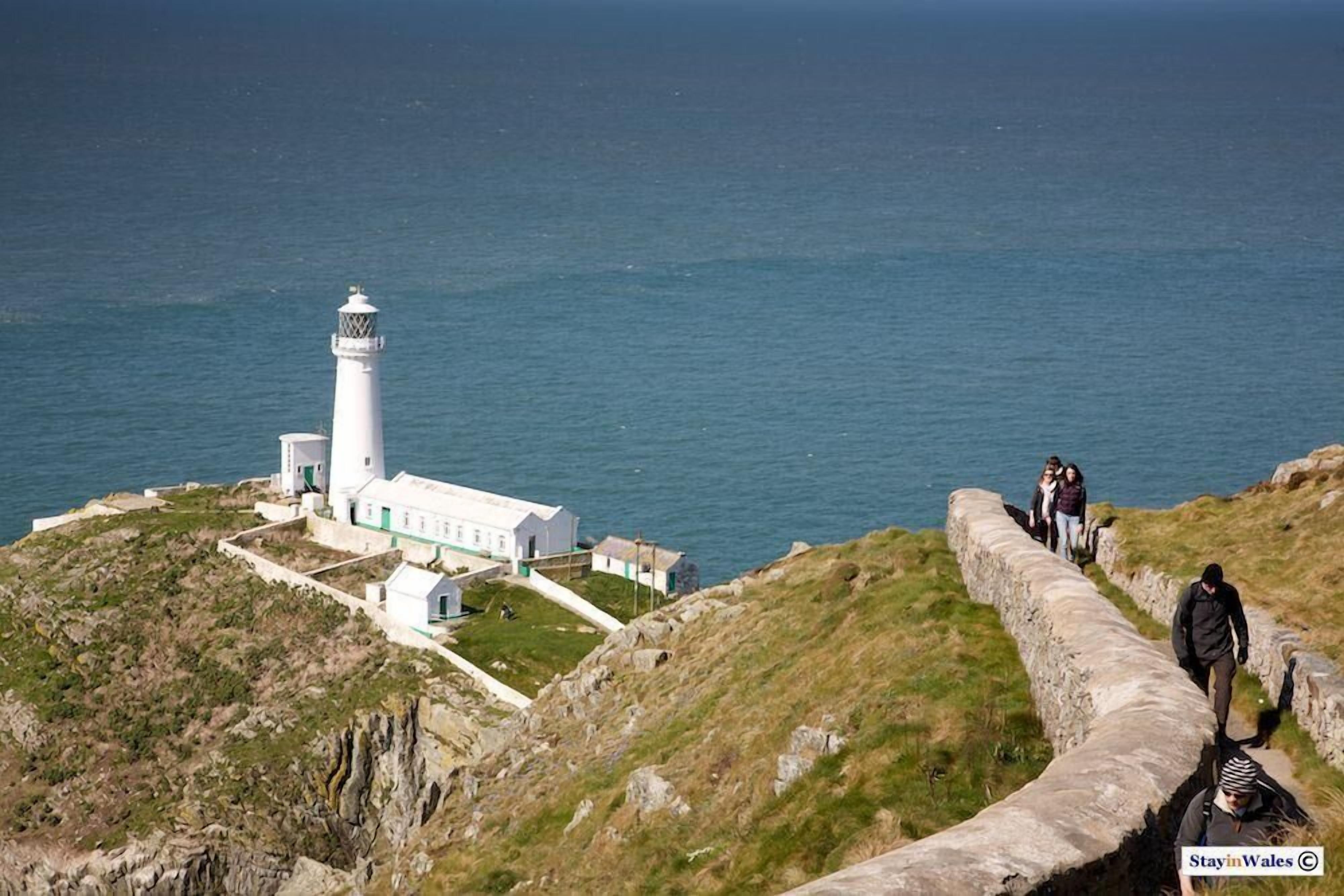 A lighthouse on a cliff with a stone wall and a grassy area.