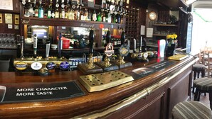 A bar area with multiple taps, a menu board, and a view of the restaurant in the background. - The Trecastell Hotel (Amlwch)