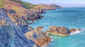 A coastal landscape with rocky cliffs and clear blue waters. - The Trecastell Hotel (Amlwch)