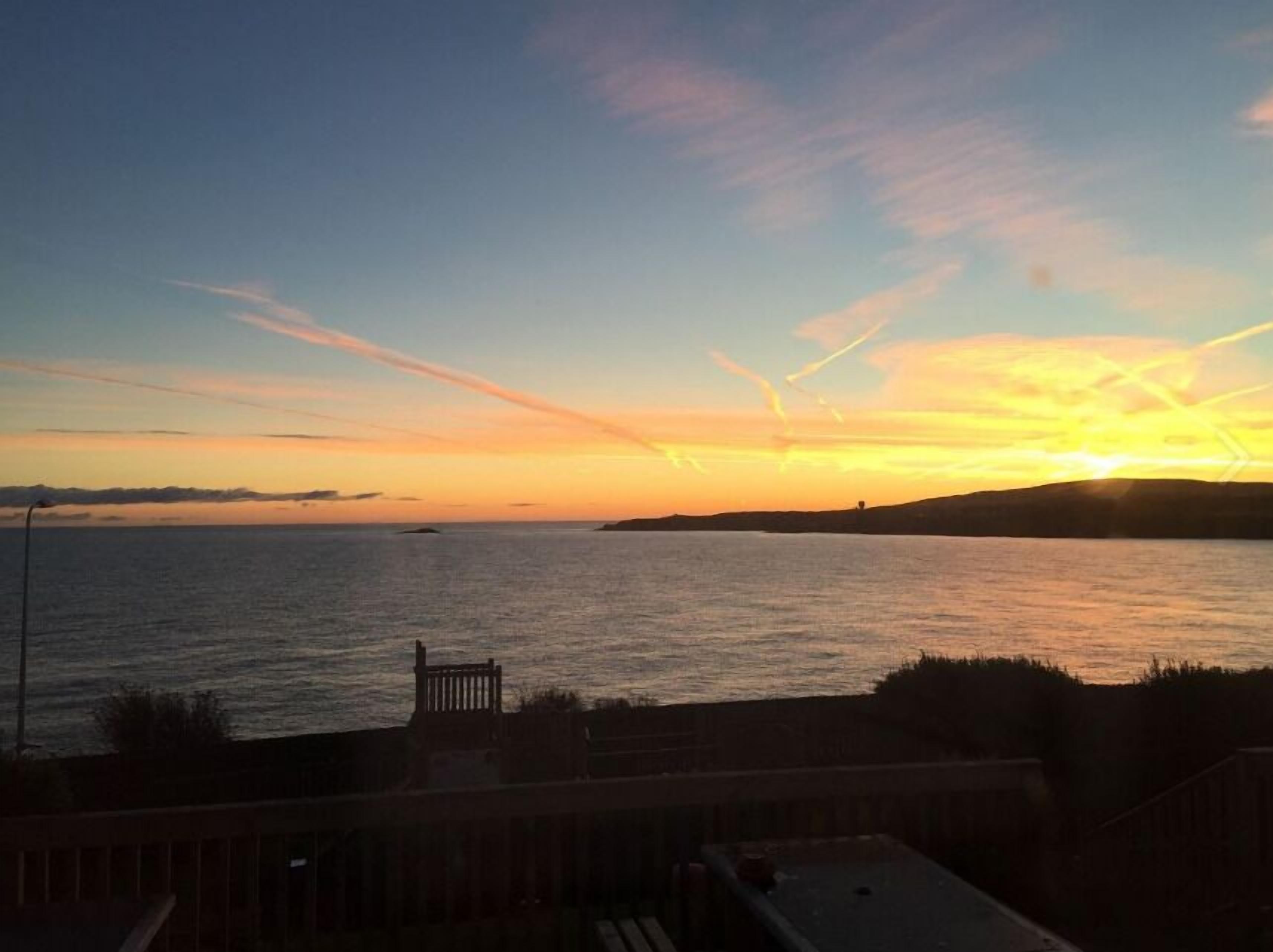A sunset view from a balcony overlooking a calm sea with distant landforms.