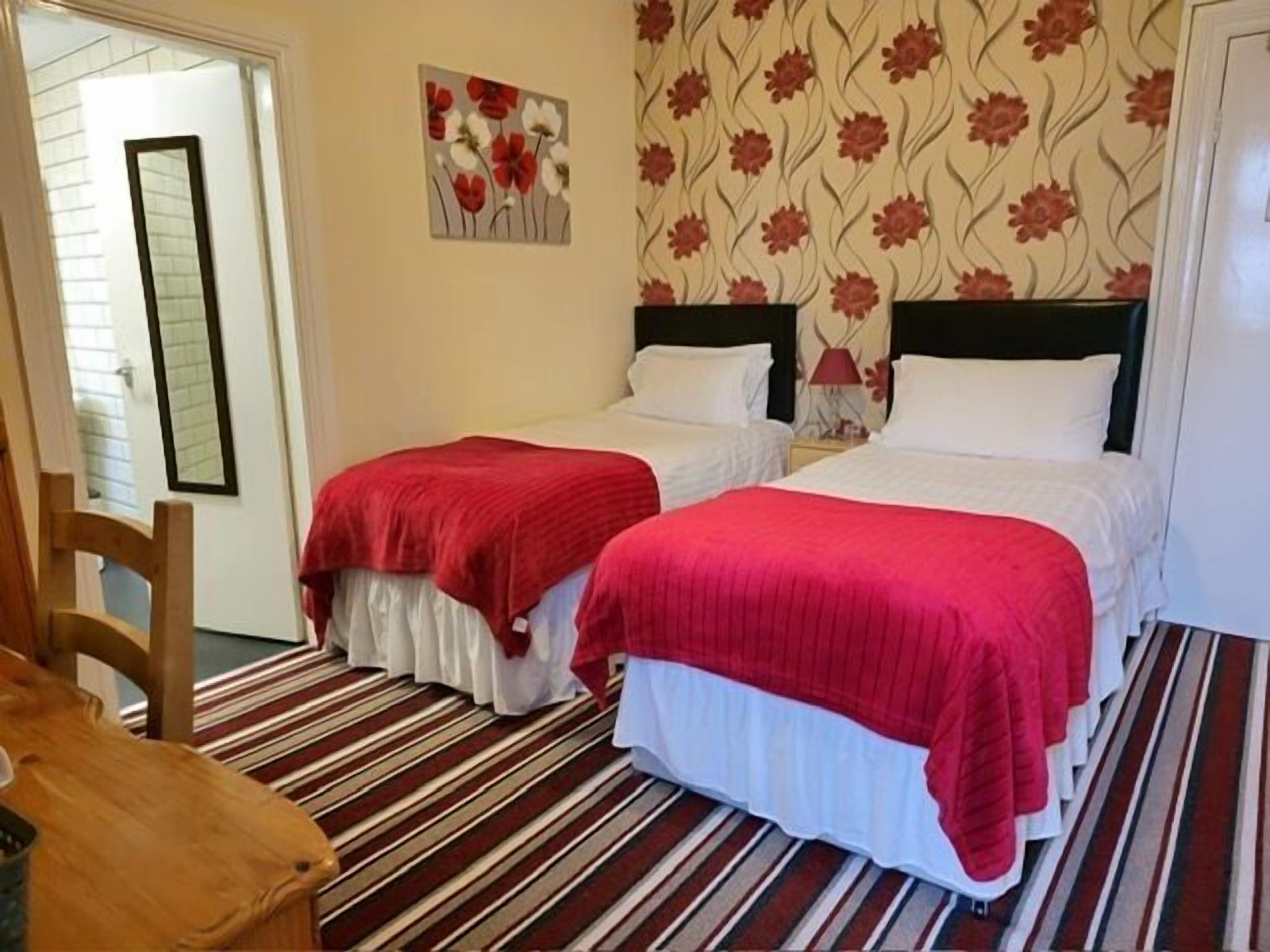 A hotel room with two beds, a striped carpet, floral wallpaper, and a wooden chair.