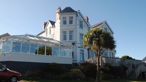 A large, two-story building with a conservatory, a staircase, and a palm tree in the foreground. - The Trecastell Hotel (Amlwch)
