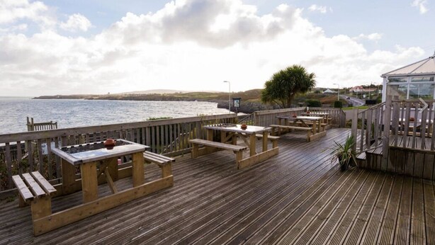 A wooden deck with picnic tables and benches overlooking the sea. - The Trecastell Hotel (Amlwch)