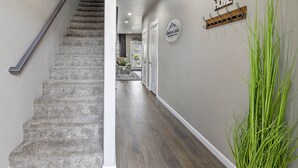 A hallway with a carpeted staircase, a 'Home' sign, and a plant. - Serenity-Themed, Fastest WiFi, 2 King Beds Home (Medford)
