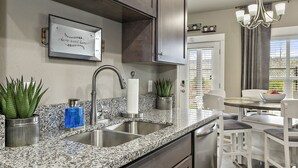 A modern kitchen with granite countertops, stainless steel appliances, and a dining area with a white table and chairs. - Serenity-Themed, Fastest WiFi, 2 King Beds Home (Medford)