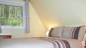 Un dormitorio con cama, una ventana con cortinas, una mesita de noche y una lámpara.