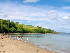 A beach with people walking along the shore, a grassy hill in the background, and a body of water.