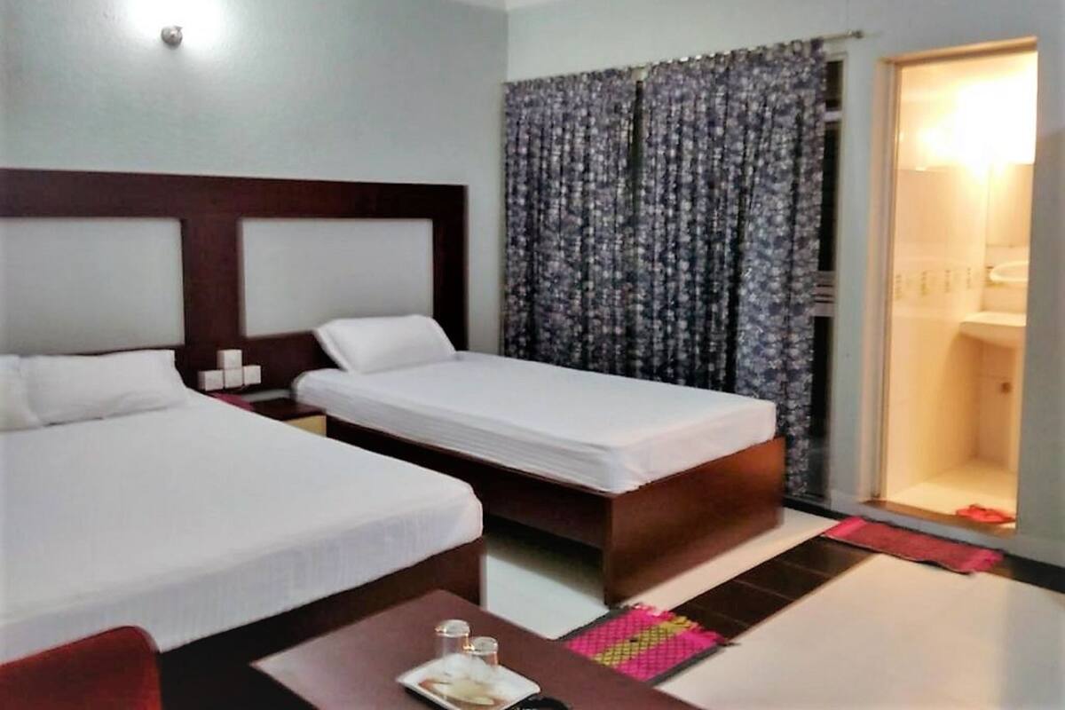 Habitación de hotel con dos camas individuales, una mesita con un plato y vasos, una silla roja y un baño visible a través de una puerta de cristal.