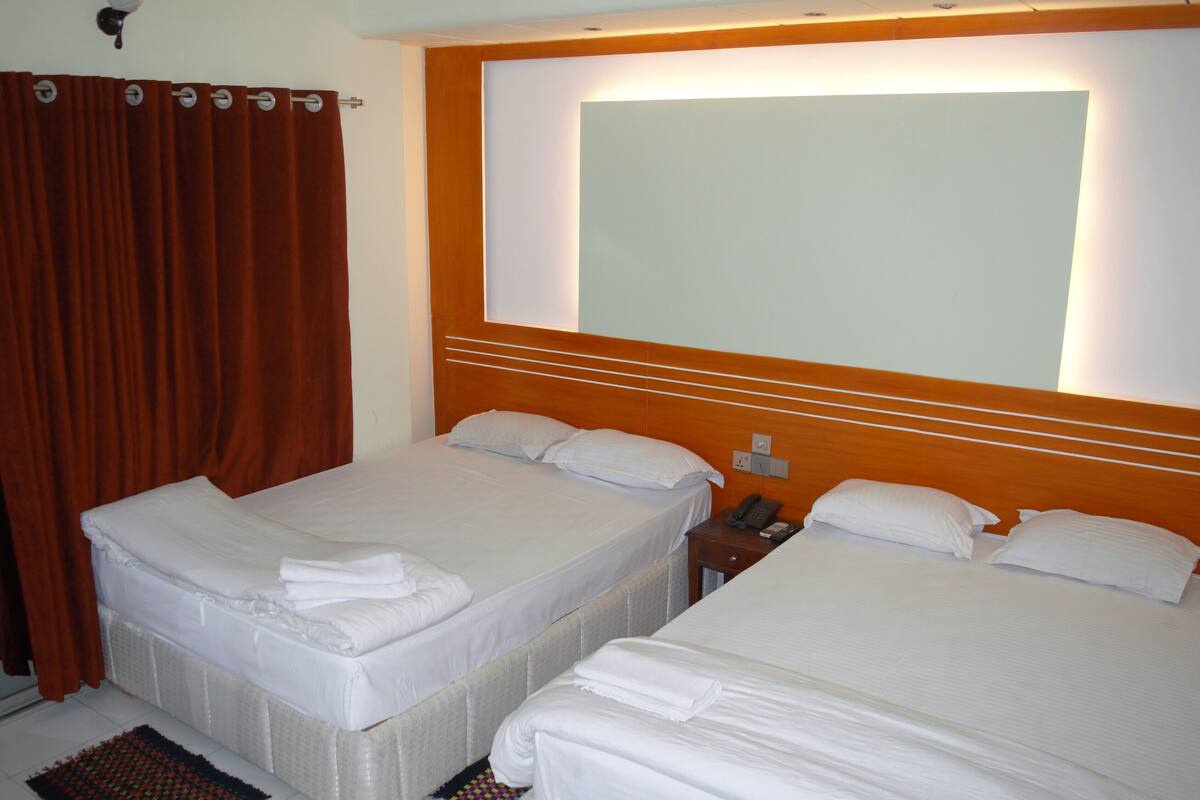 Habitación de hotel con dos camas, un cabecero de madera, un teléfono y una cortina.