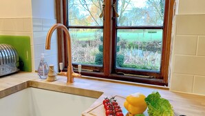 Een keuken met een gootsteen, een raam met uitzicht op groen, een groen apparaat en een snijplank met groenten.