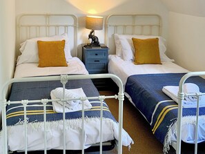 Two twin beds with white and blue bedding, a nightstand with a lamp, and a small statue.