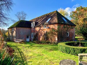 A brick house with a sloped roof, a visible satellite dish, and a well-maintained lawn with a bench.