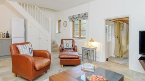 Een woonkamer met een bank, fauteuil, salontafel en een trap die naar een keuken leidt.